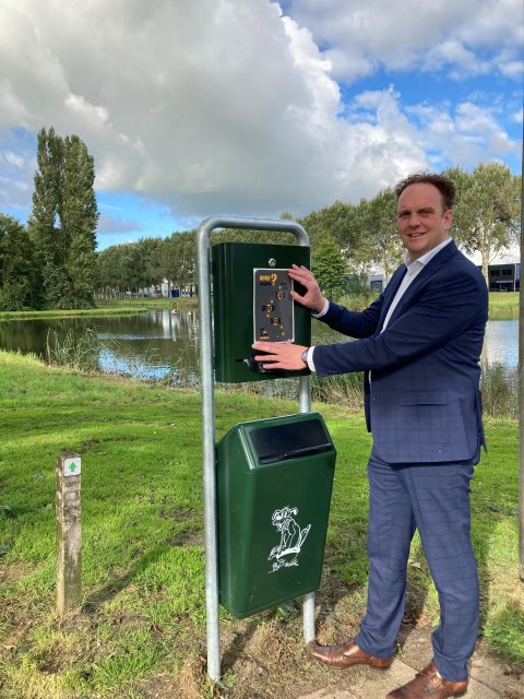 afbeelding wethouder Slingerland bij afvalbak met dispenser voor hondenpoep